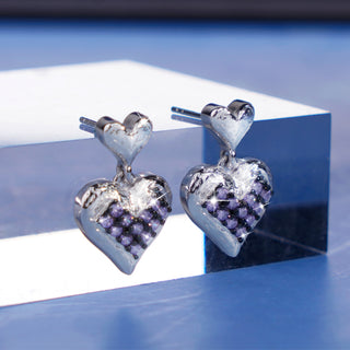 Heart-shaped earrings with purple gemstones on a reflective surface