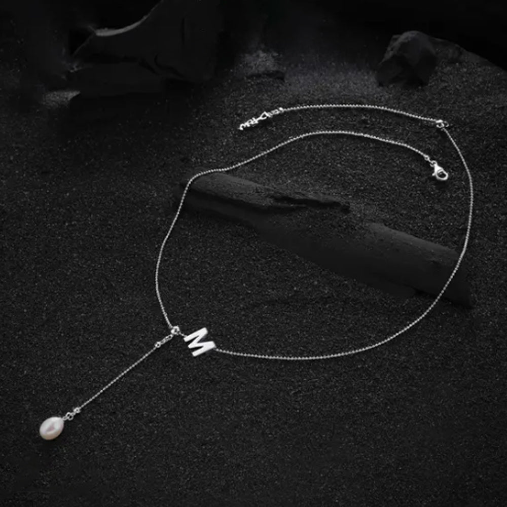 Letter "M" pendant from the cream-colored necklace, highlighted for its smooth finish and refined design.