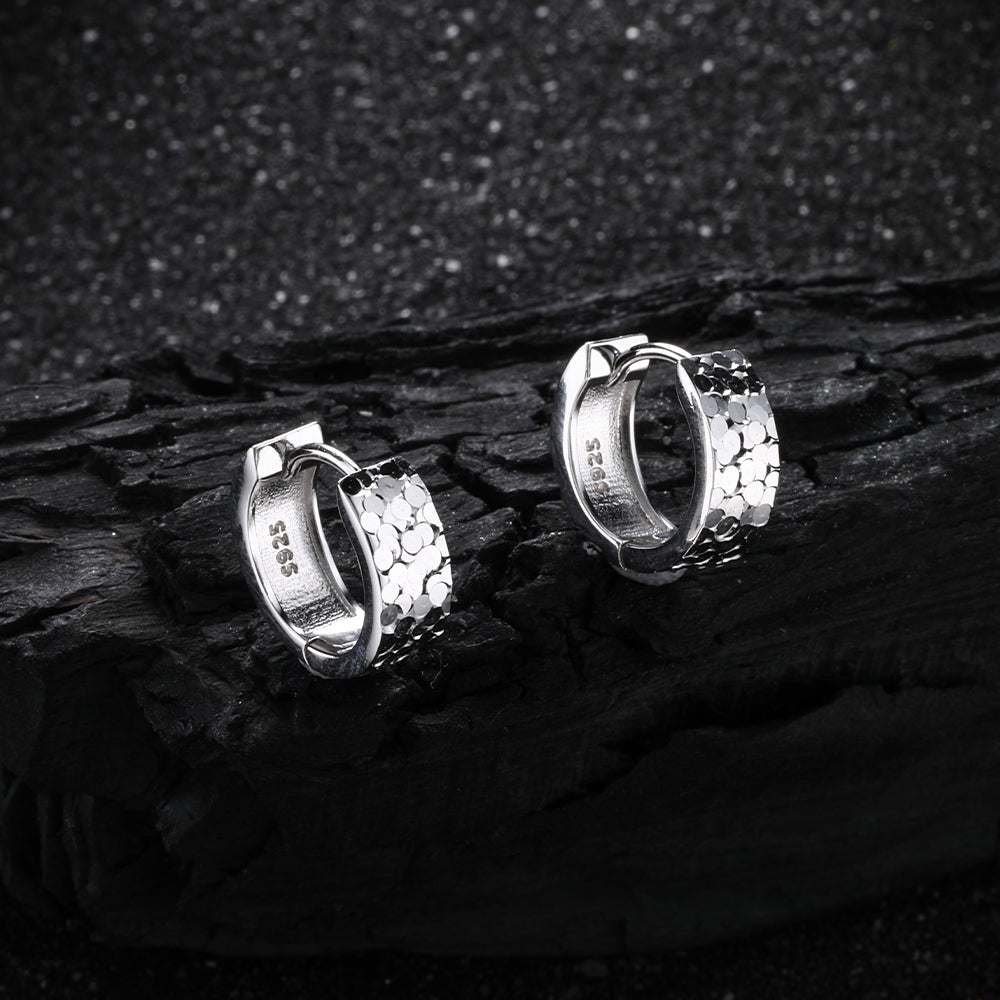 A pair of D-POW hammered sterling silver ear cuffs displayed on a black background, emphasizing the unique texture and sleek design in a bold contrast.