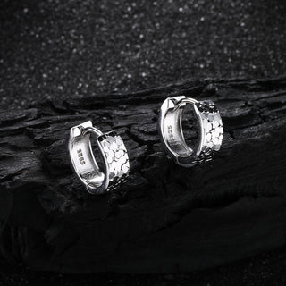 A pair of D-POW hammered sterling silver ear cuffs displayed on a black background, emphasizing the unique texture and sleek design in a bold contrast.