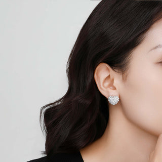 Close-up of both heart studs worn by model, showing contrast between silver finishes on each ear.